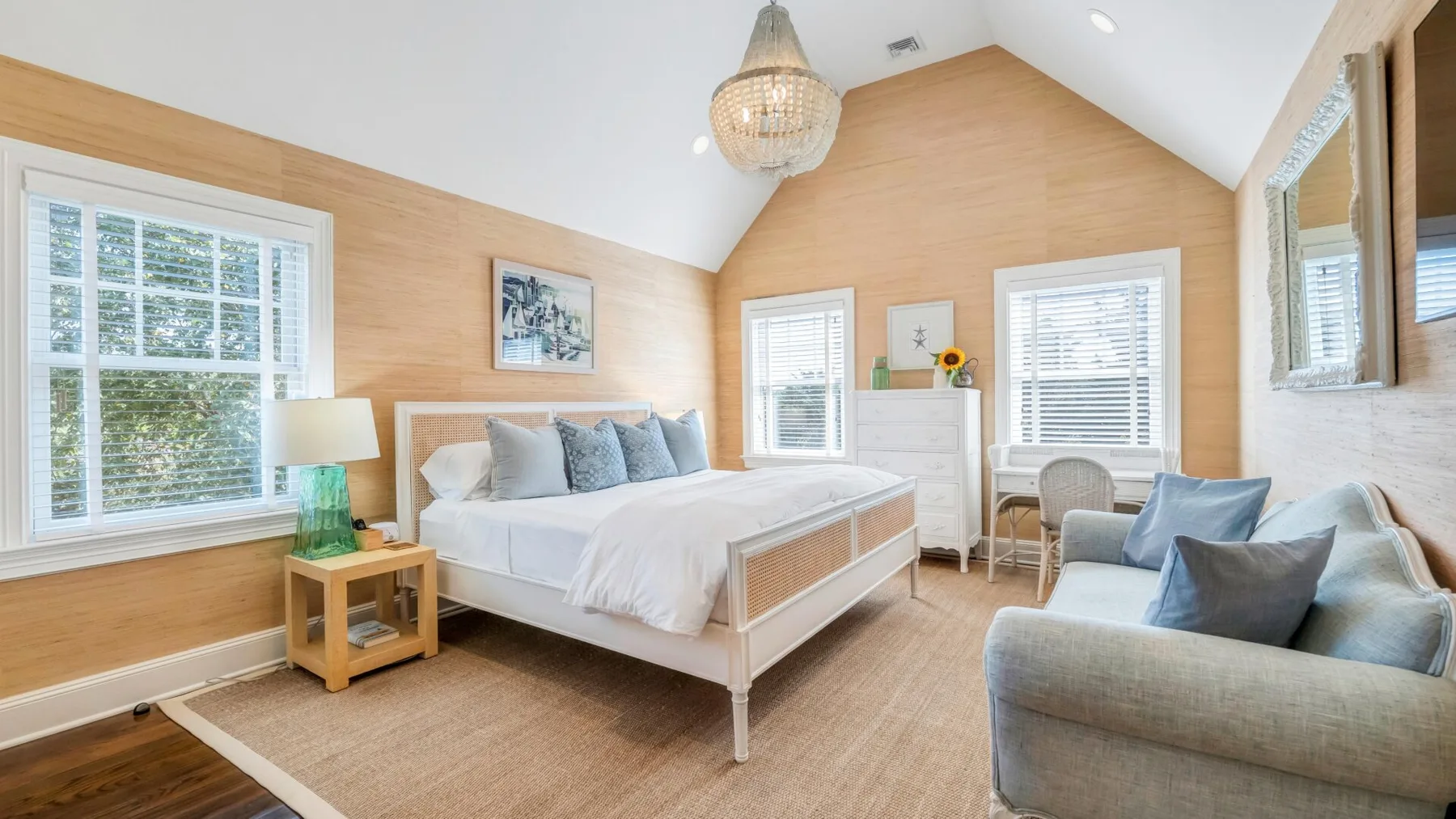 A bright bedroom with a large bed, windows, and a seating area.