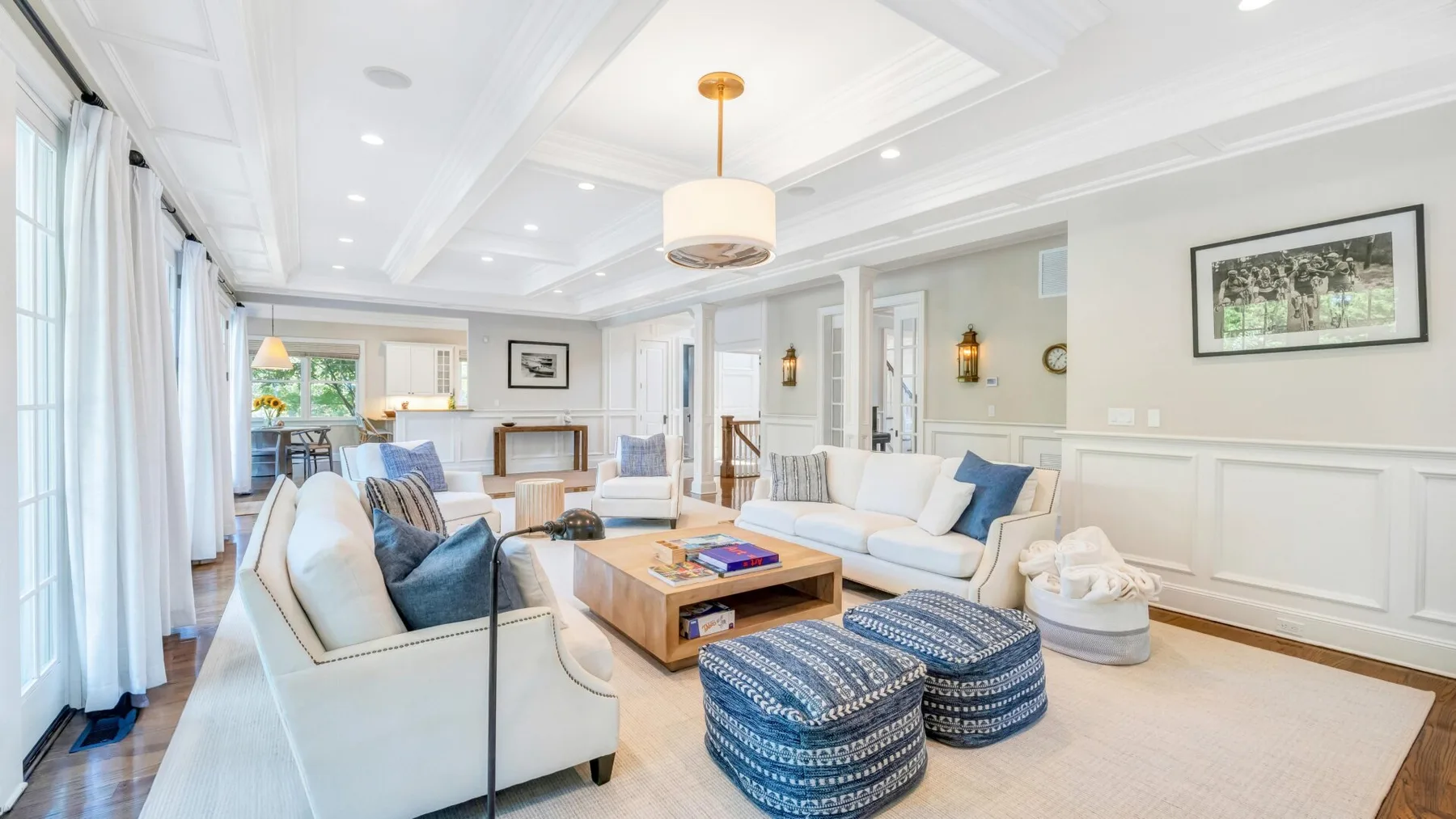A bright living room with light seating, blue ottomans, and a wooden coffee table.