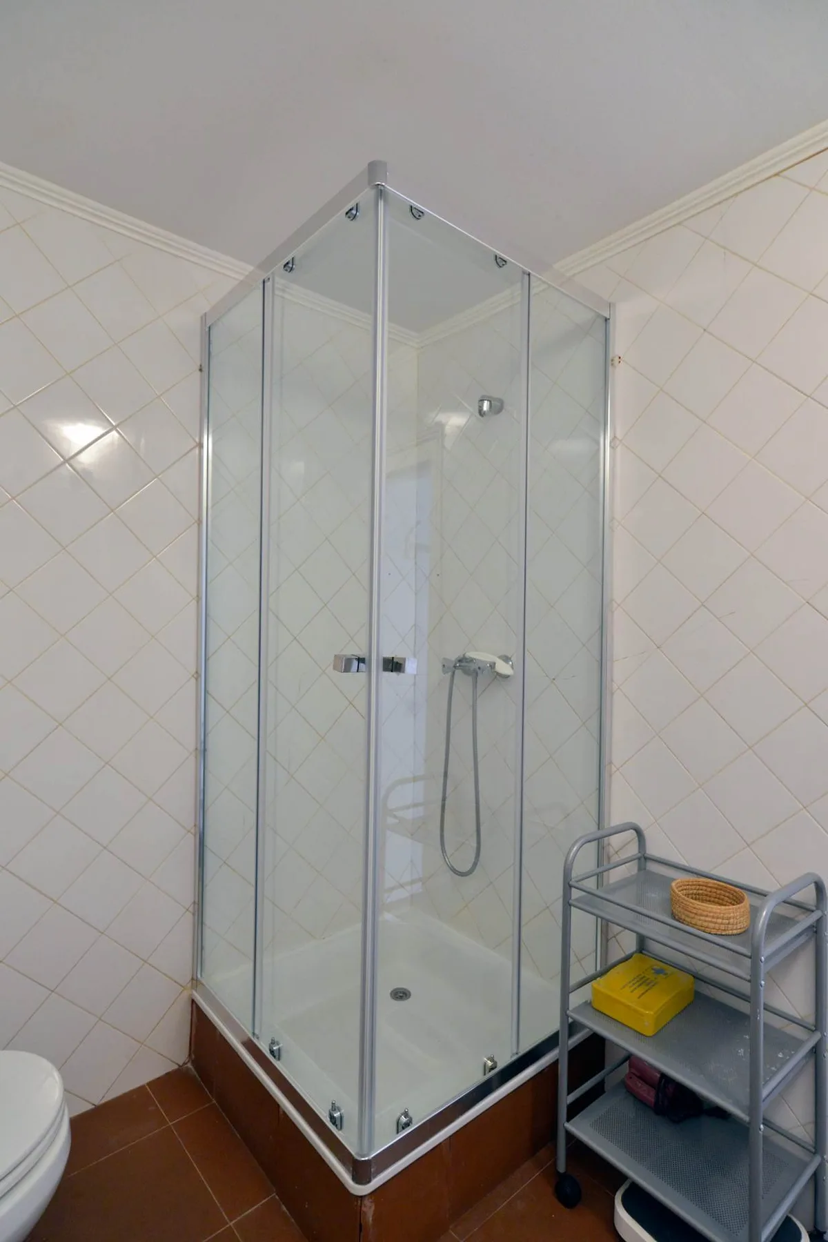 A tiled bathroom with a glass shower and a small storage cart.