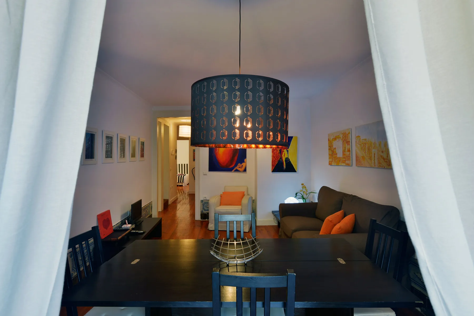 A dining table faces a living area with seating and colorful wall art.
