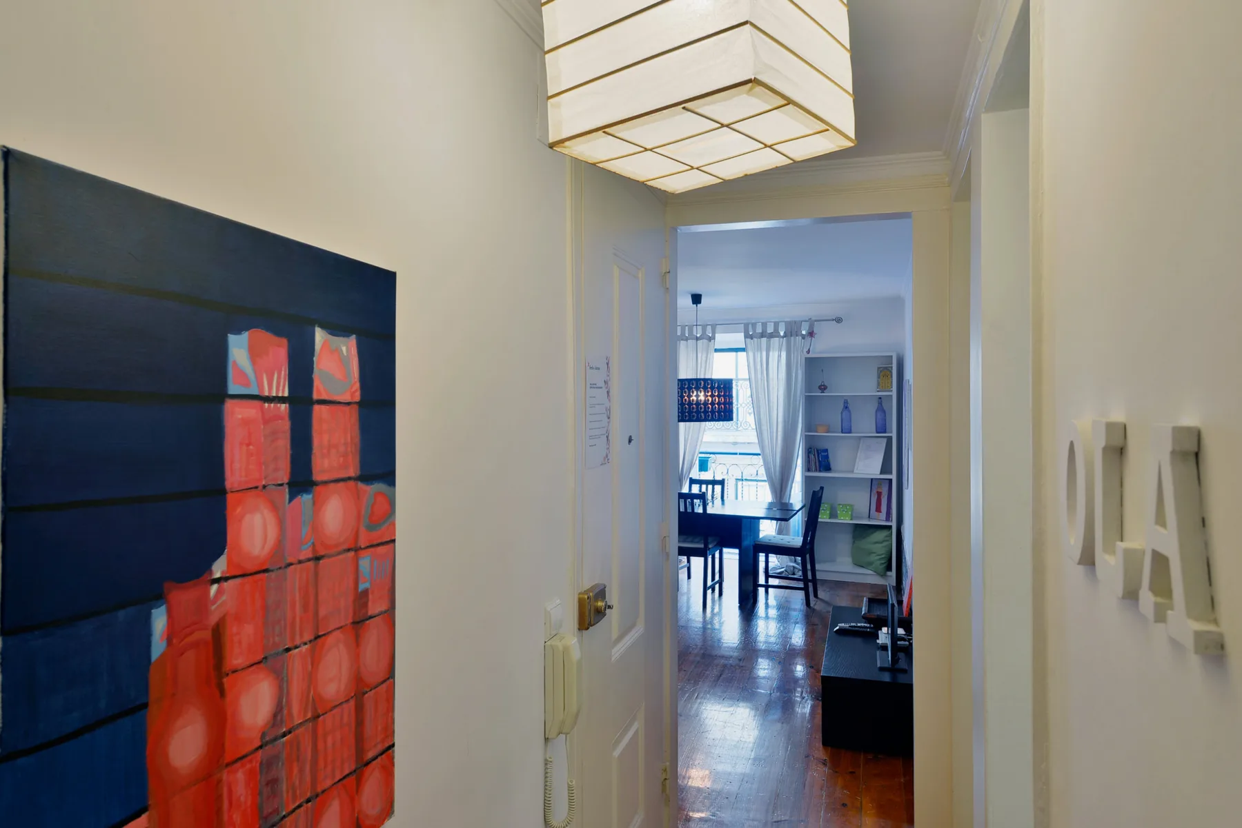A hallway with a large red-and-black artwork leads into a bright living area.