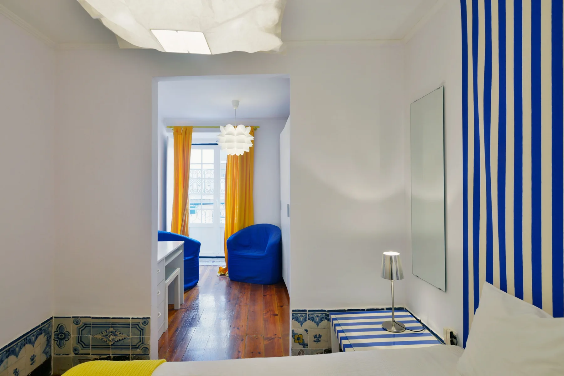A bedroom opens into a sitting area with blue seating and striped curtains.