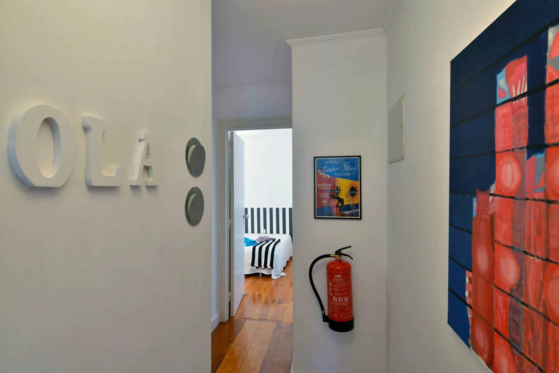 A hallway with wall art and a fire extinguisher beside an open bedroom doorway.