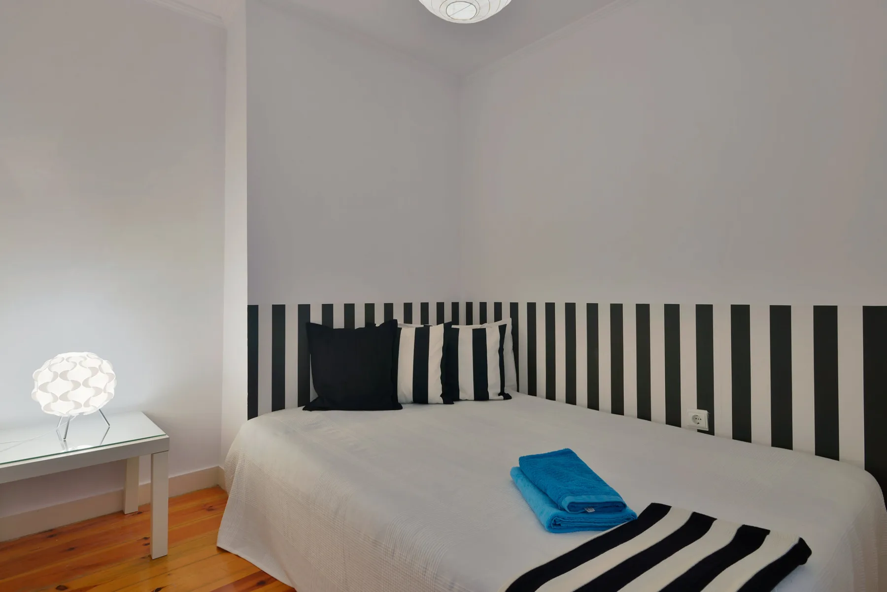 A bedroom with a bed, striped headboard, and folded blue towel.