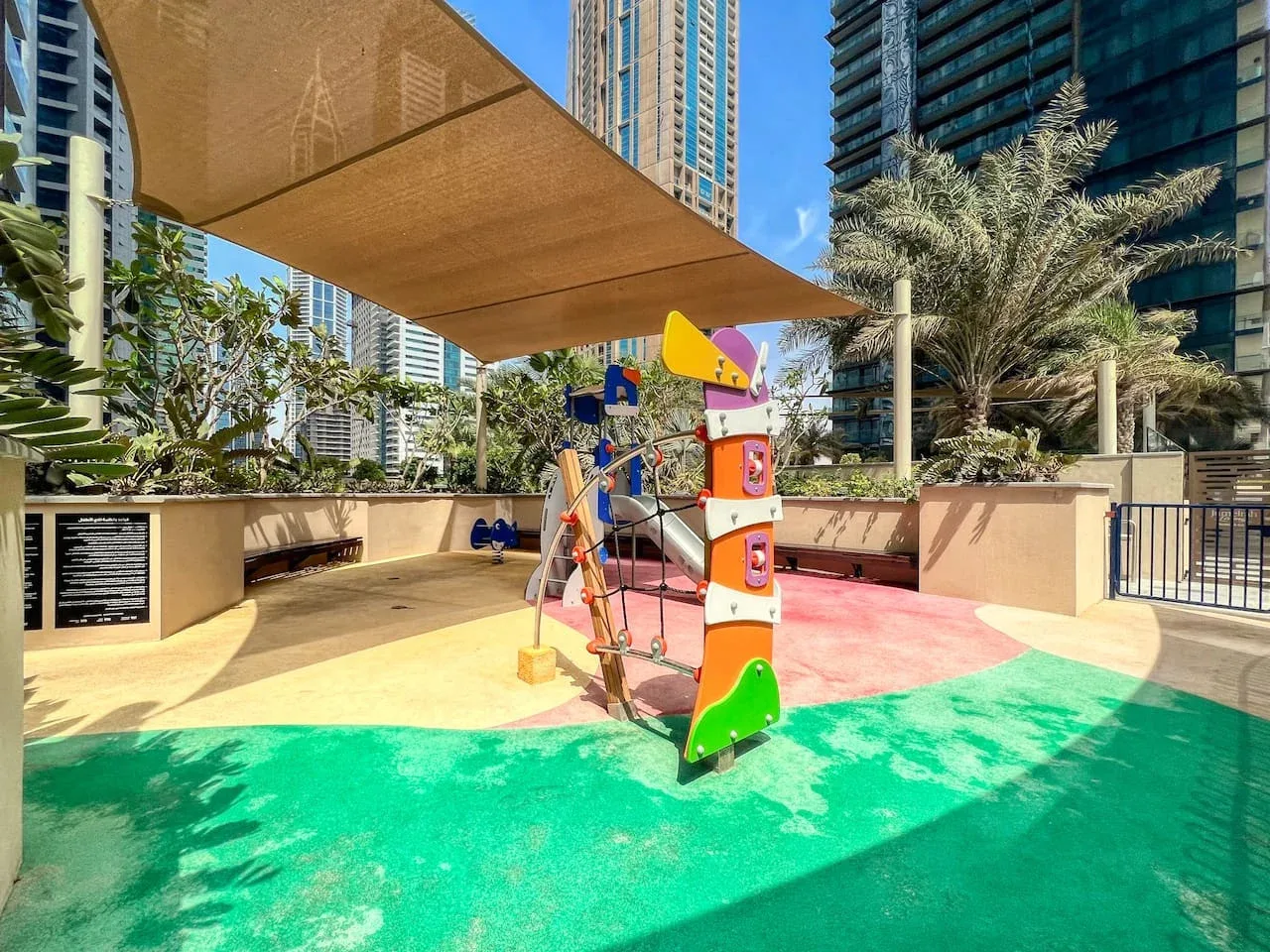 Un área de juegos al aire libre con equipo colorido bajo una cubierta de sombra.