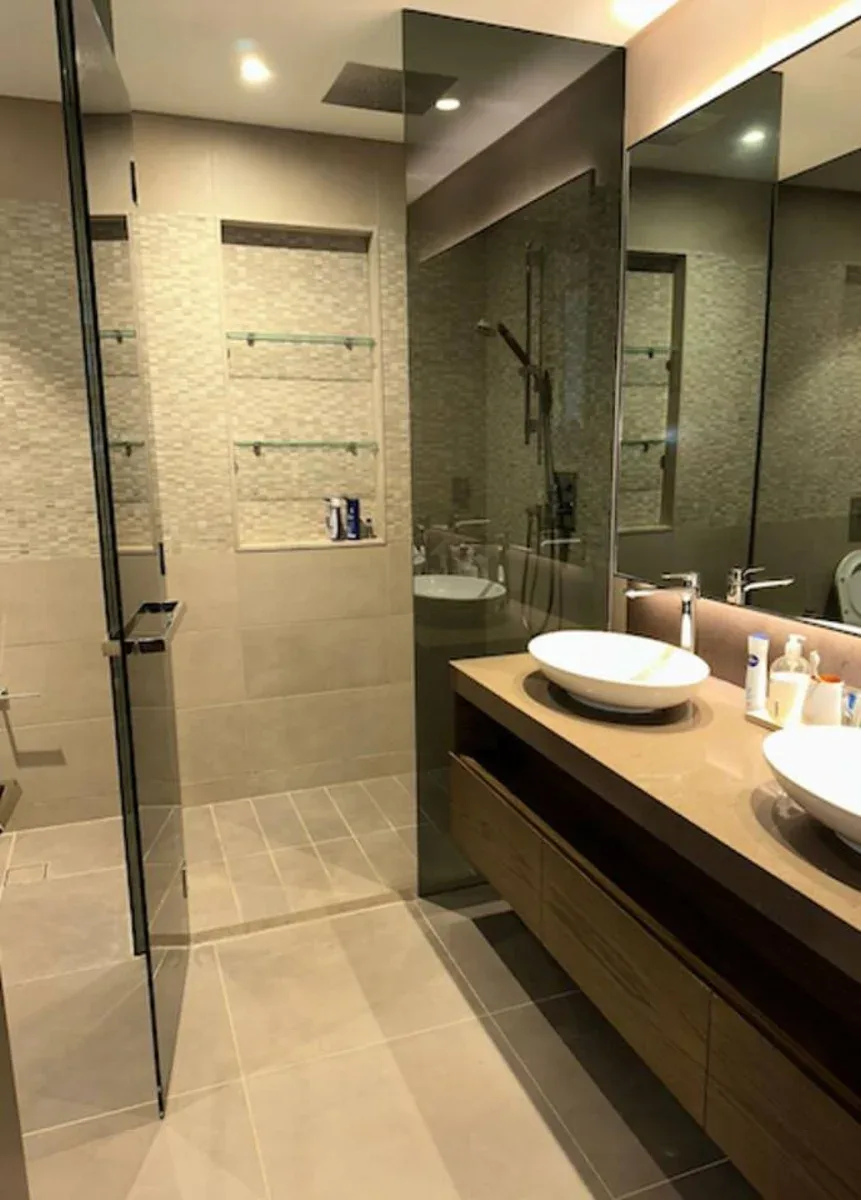 Un baño moderno con una ducha de vidrio y un largo tocador con lavabos de sobreponer.