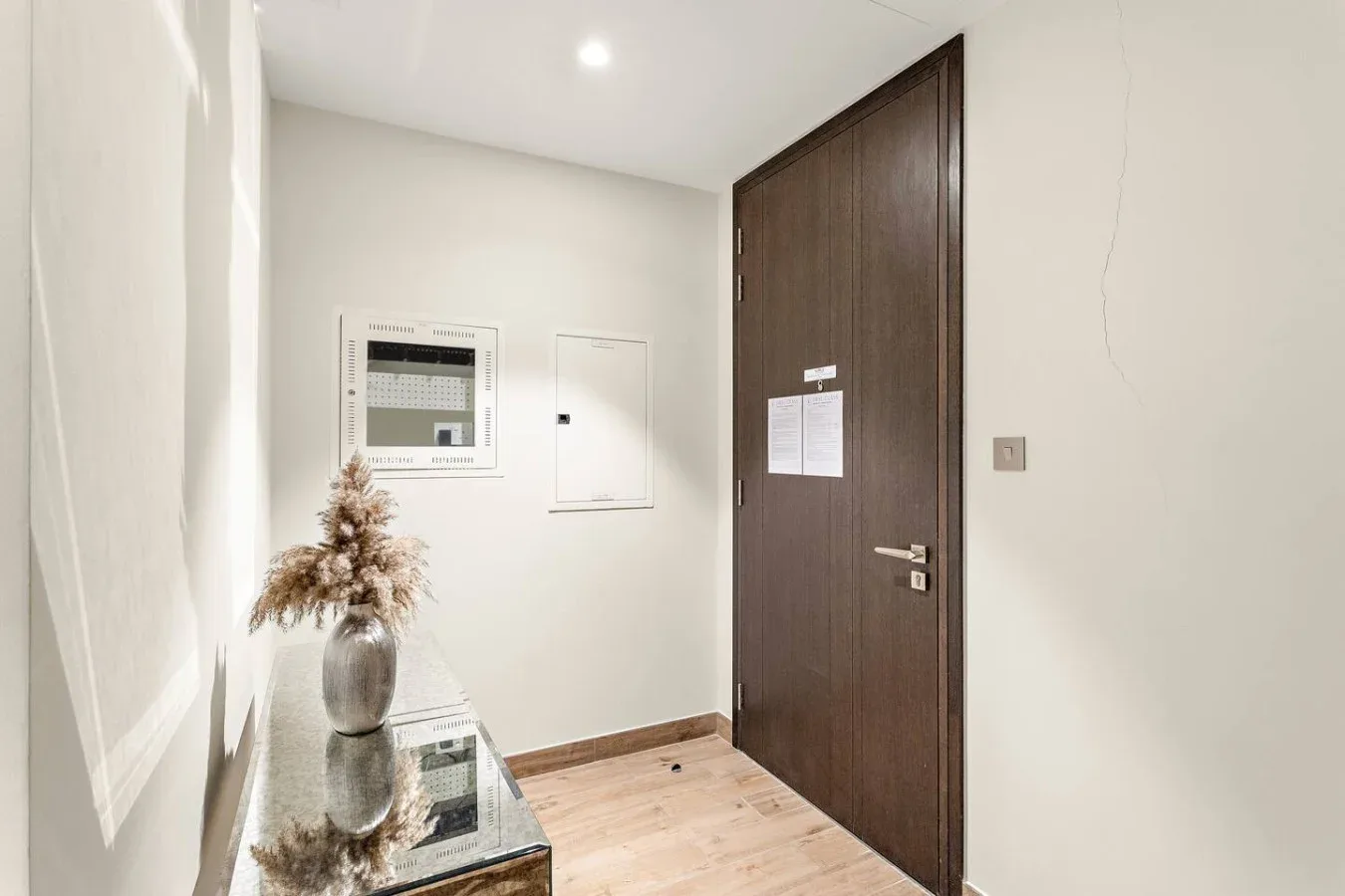Una entrada luminosa con una puerta de madera oscura y una pequeña mesa con tapa de vidrio.