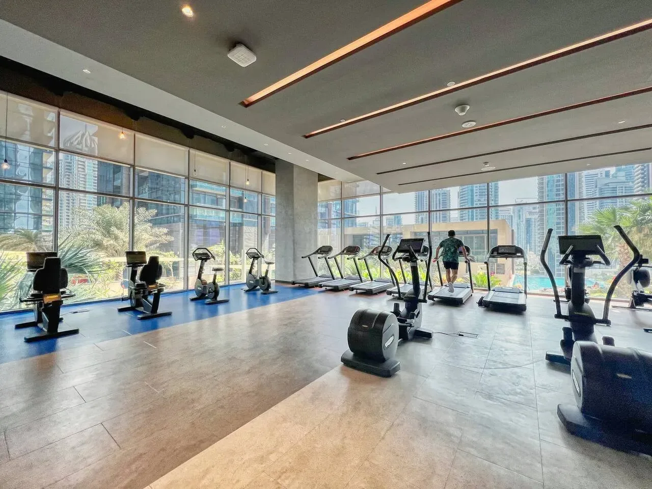 Un gimnasio con máquinas de ejercicio junto a grandes ventanales con edificios a la vista.