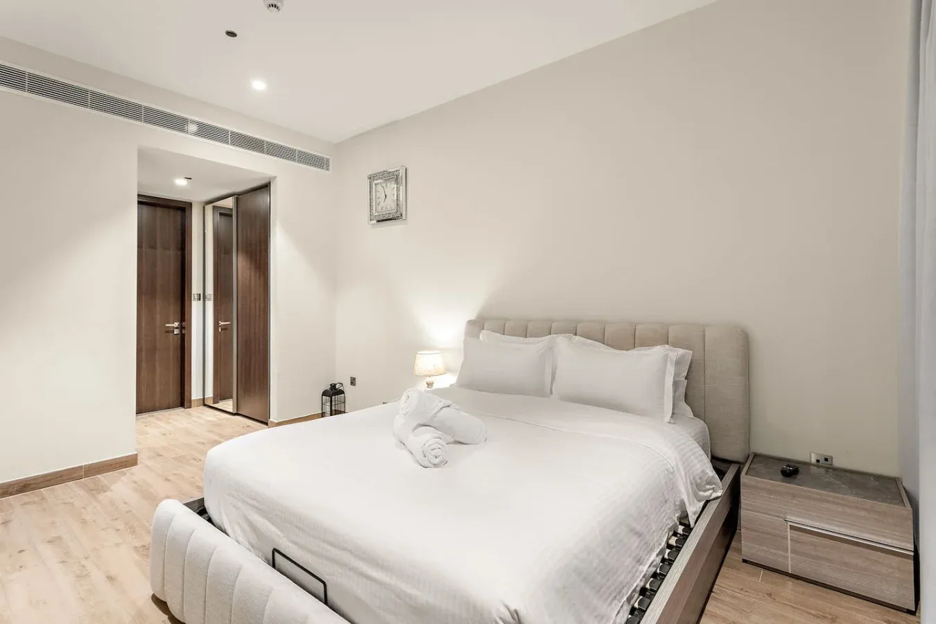 Un dormitorio luminoso con una cama bien arreglada y suelo de madera clara.