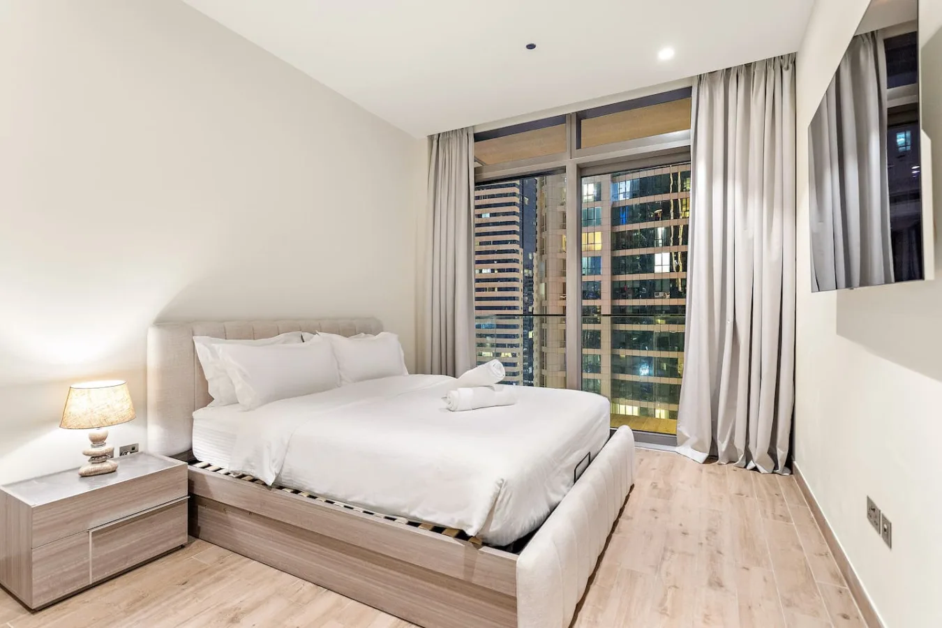 Un dormitorio luminoso con una cama grande junto a ventanas de suelo a techo.
