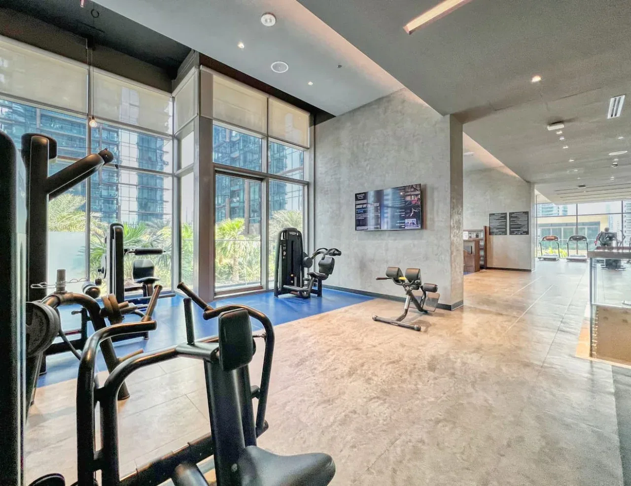 Un gimnasio luminoso con máquinas de ejercicio junto a grandes ventanas.