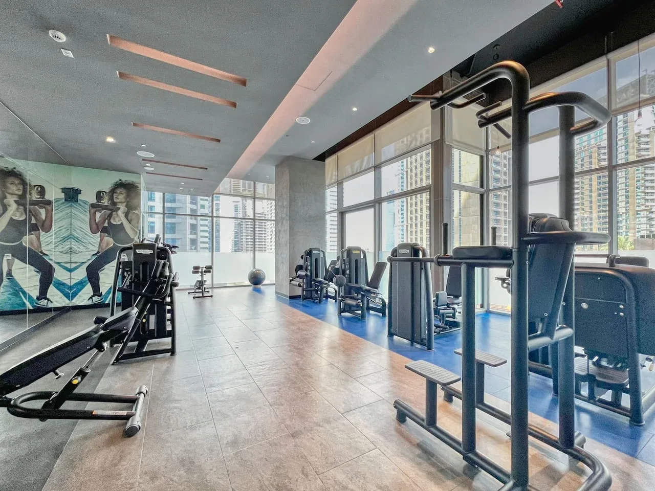 Un gimnasio con máquinas de ejercicio junto a grandes ventanales.