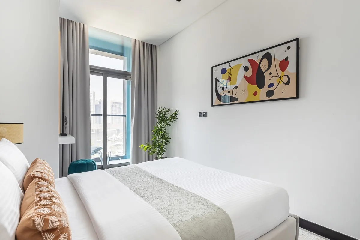 Un dormitorio luminoso con una cama tendida y arte abstracto colorido en la pared.