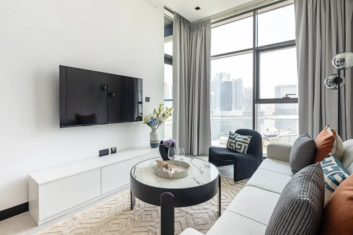Una sala luminosa con televisión, asientos y grandes ventanales con vistas a la ciudad.