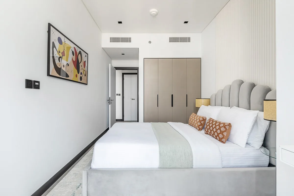 Un dormitorio luminoso con una cama tendida y armarios empotrados.