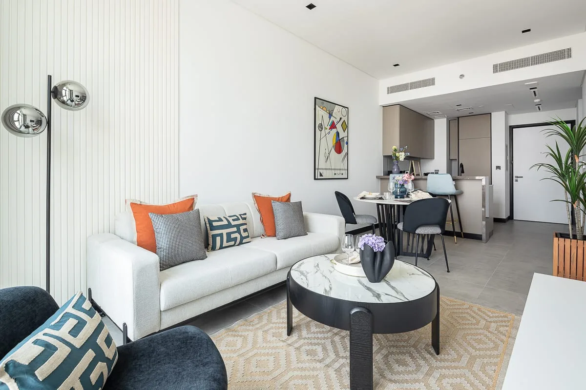 A bright living room with a white sofa, round coffee table, and open kitchen.