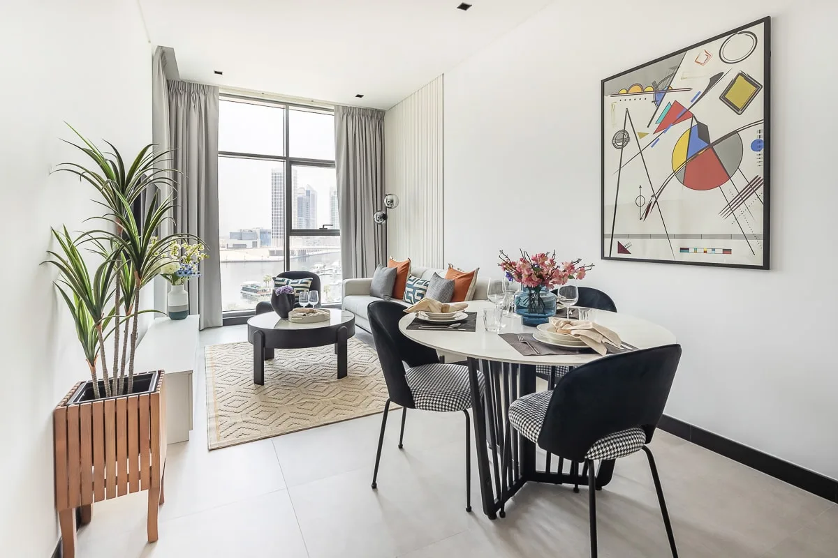 A bright dining area with a set table beside a living area and large windows.