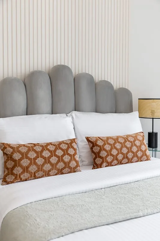Un dormitorio con una cama vestida con ropa blanca y cojines estampados color óxido.