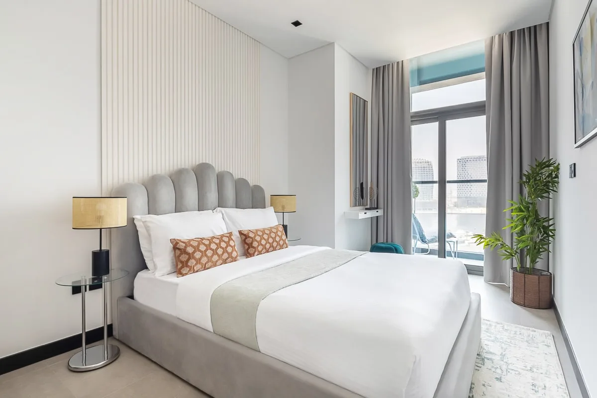 Un dormitorio luminoso con una cama grande y ventanas altas.