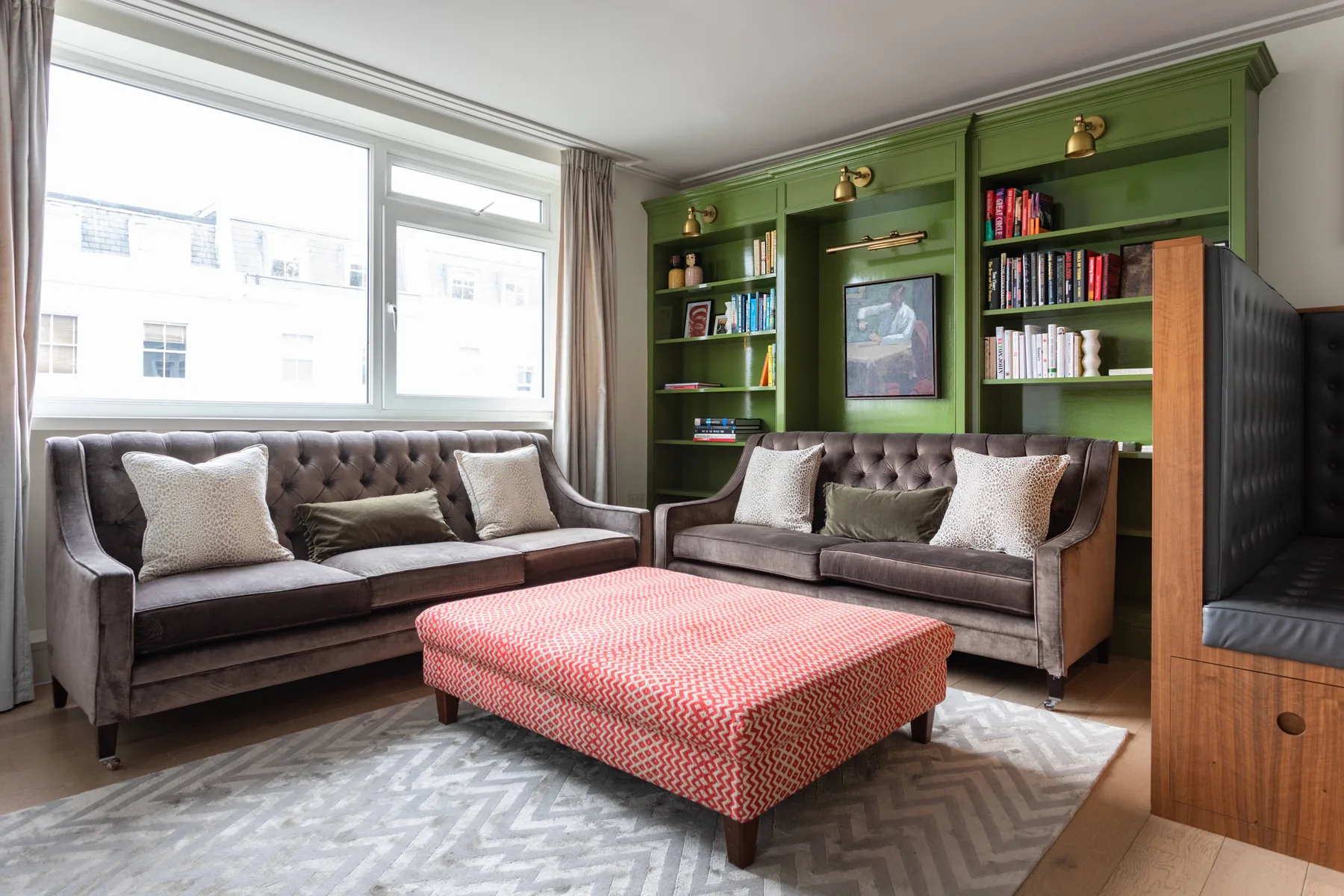 A living room with seating around a red patterned ottoman and green built-in bookshelves.