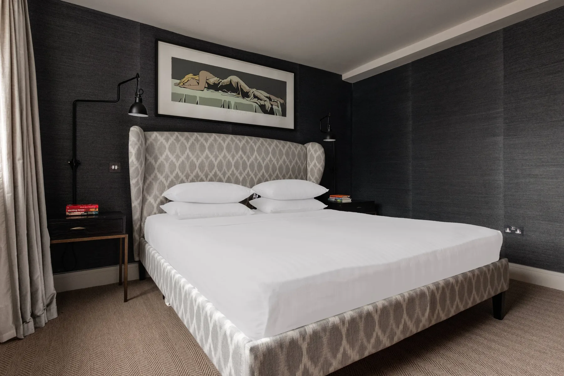 A bedroom with a large bed, dark walls, and framed artwork above the headboard.