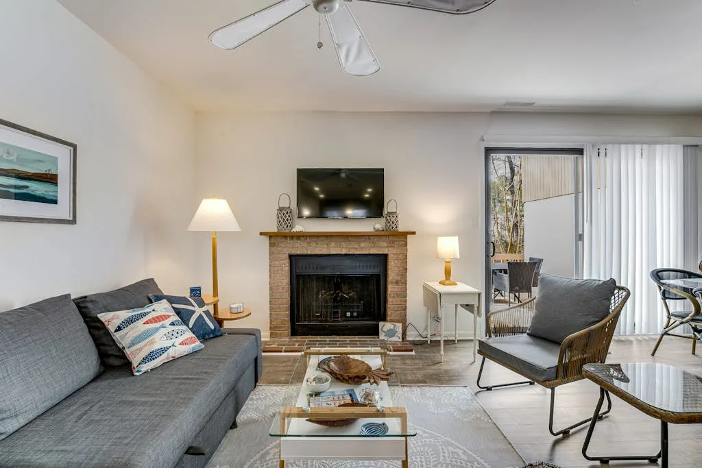 A living room with a gray sofa and a brick fireplace beneath a television.