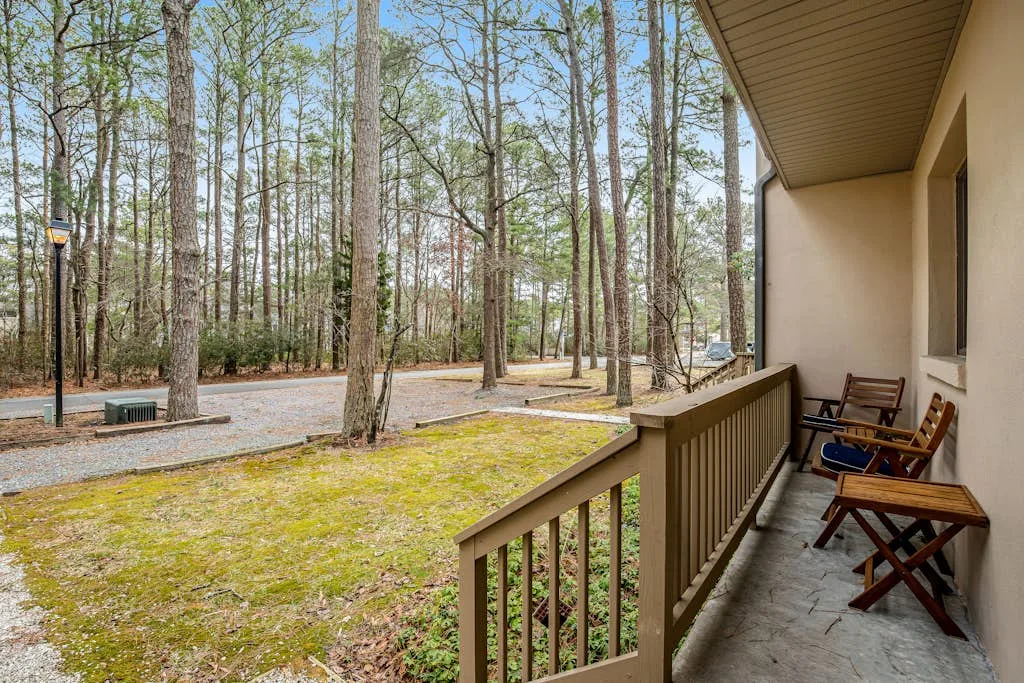 A covered porch with outdoor seating overlooks a wooded area.