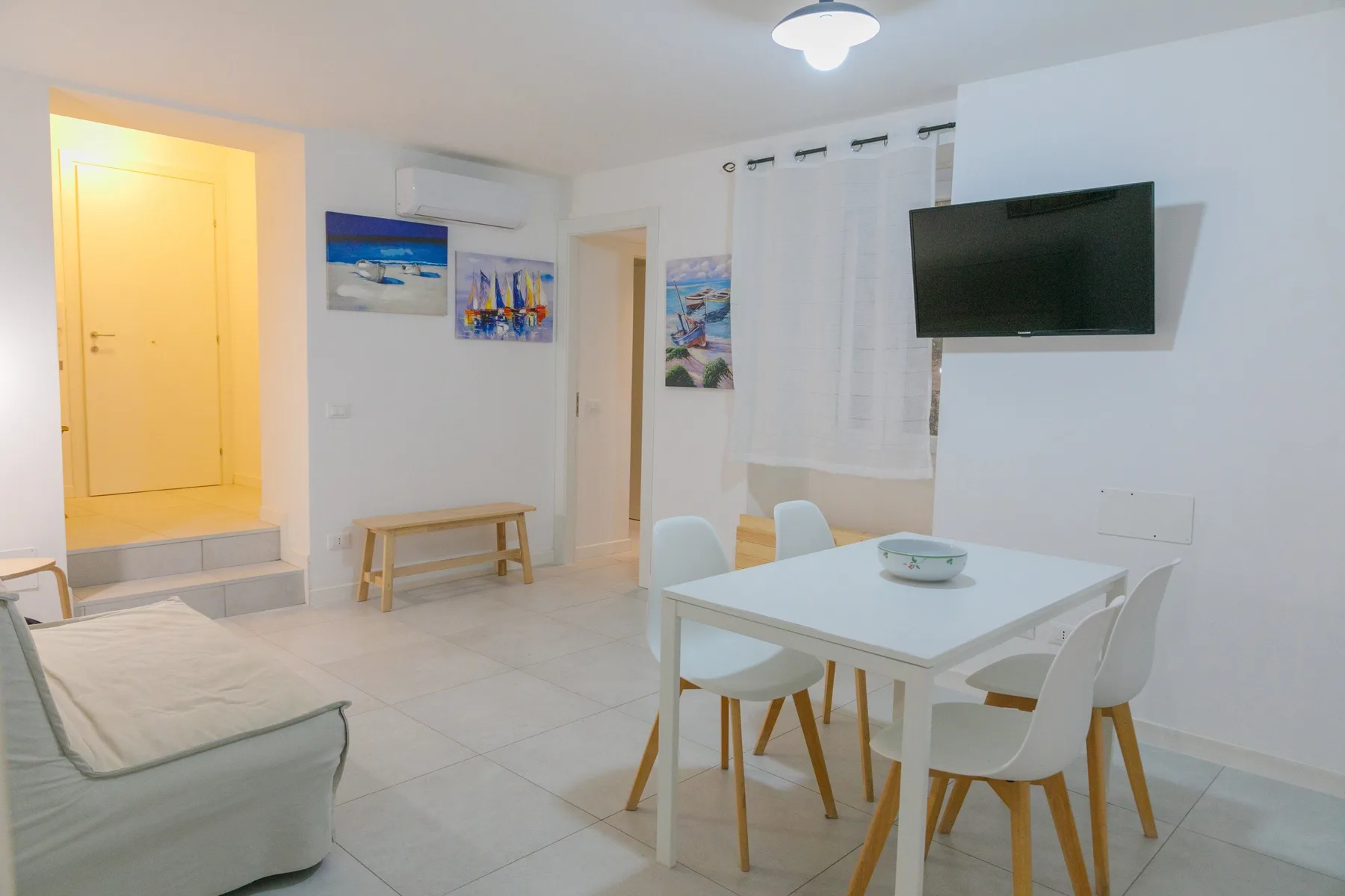 Una luminosa sala de estar y comedor con mesa, asientos y un televisor en la pared.