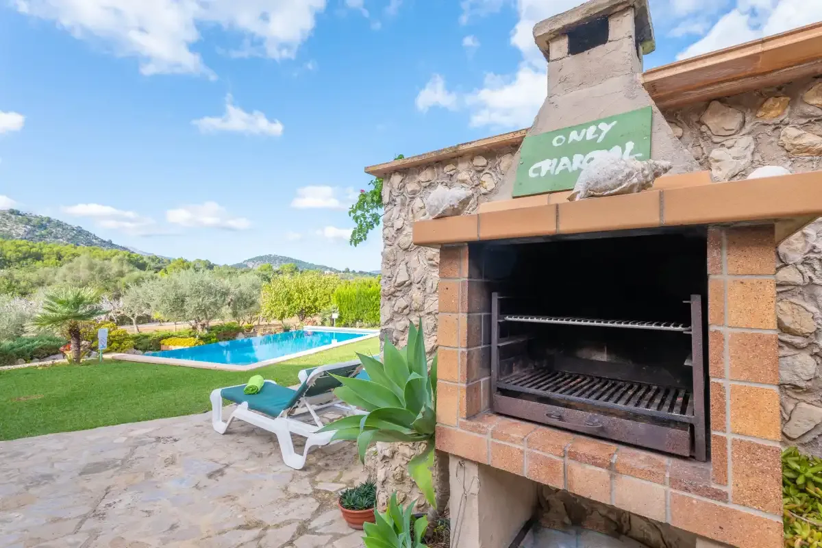 Una barbacoa de piedra al aire libre junto a una piscina y un jardín.