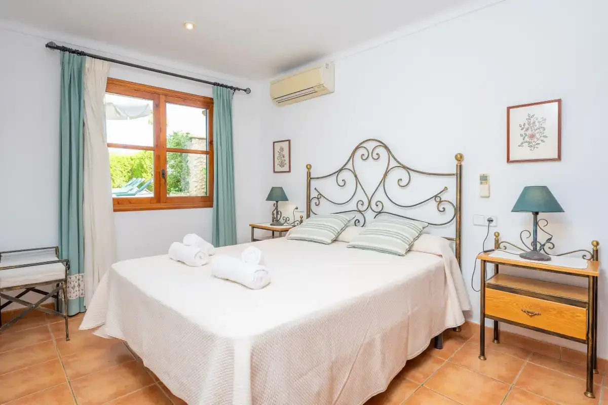 Un dormitorio luminoso con una cama doble, mesitas de noche y una ventana con cortinas.