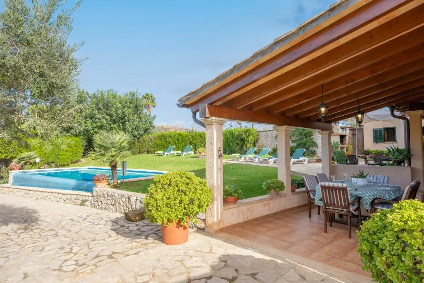 Un patio exterior cubierto con mesa de comedor da a un jardín y una piscina.