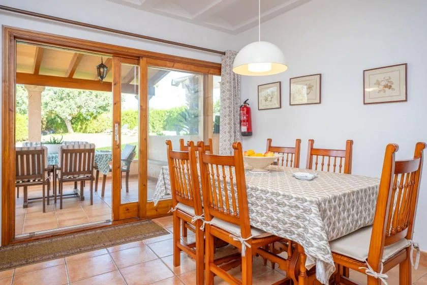 Un comedor con una mesa larga y sillas de madera junto a puertas de vidrio.