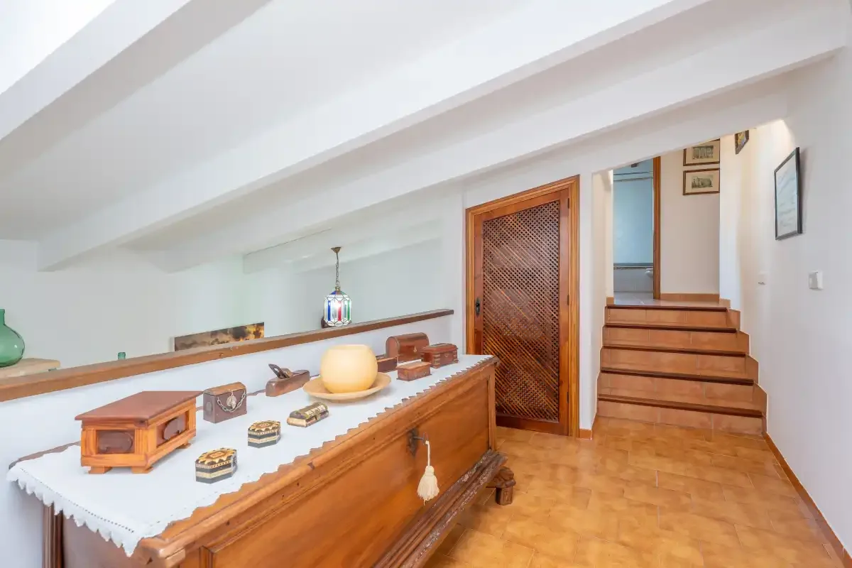 Un pasillo interior luminoso con una consola de madera y escaleras.