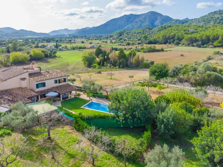 Una casa rural y una piscina dan a campos verdes y montañas lejanas.