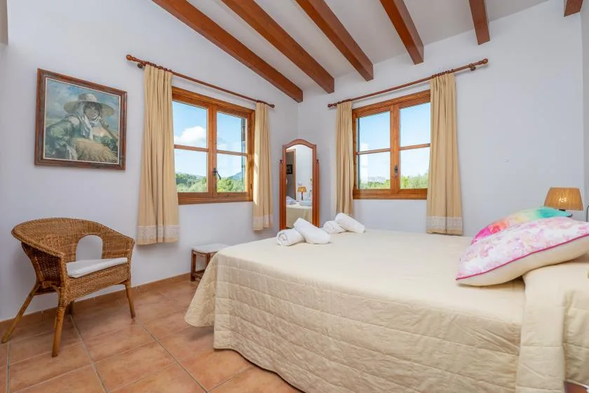 Un dormitorio luminoso con una cama grande, vigas de madera y dos ventanas.