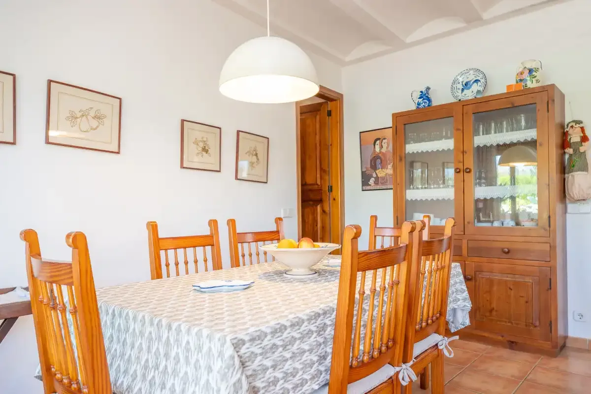 Un comedor con una mesa, asientos de madera y un armario con puertas de cristal.