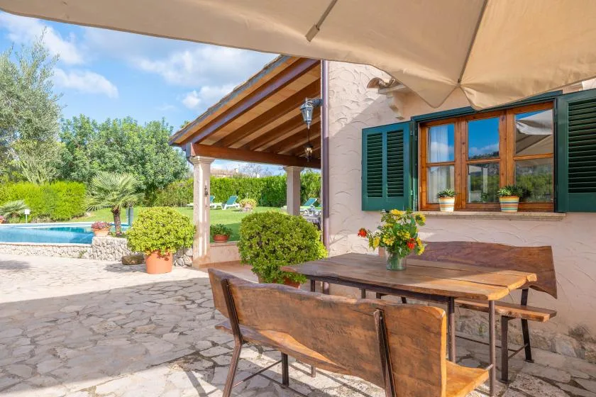 Una zona de comedor al aire libre junto a una casa de piedra, con una piscina en el jardín.