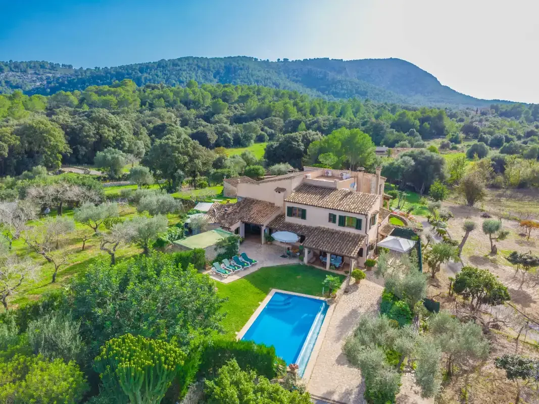 Una casa de campo con piscina está rodeada de árboles verdes y colinas.