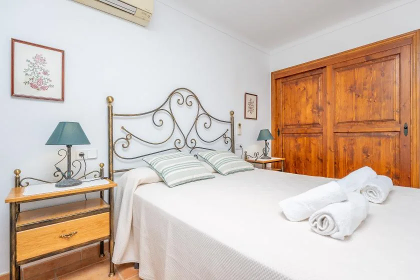 Un dormitorio con una cama de armazón metálico, mesitas de madera y un armario grande de madera.