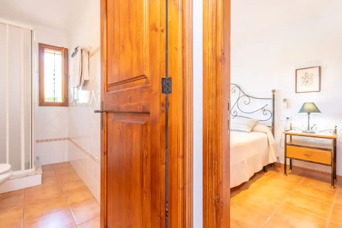 Se ve un dormitorio con cama de estructura metálica a través de una puerta de madera abierta, junto al baño.