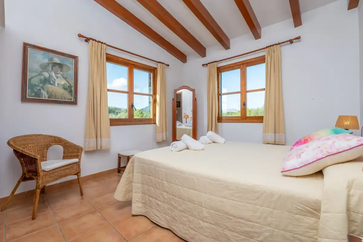Un dormitorio luminoso con una cama, dos ventanas y vigas vistas en el techo.