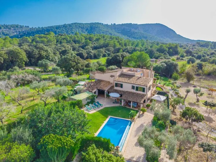 Una casa rural rodeada de vegetación, con una piscina delante.