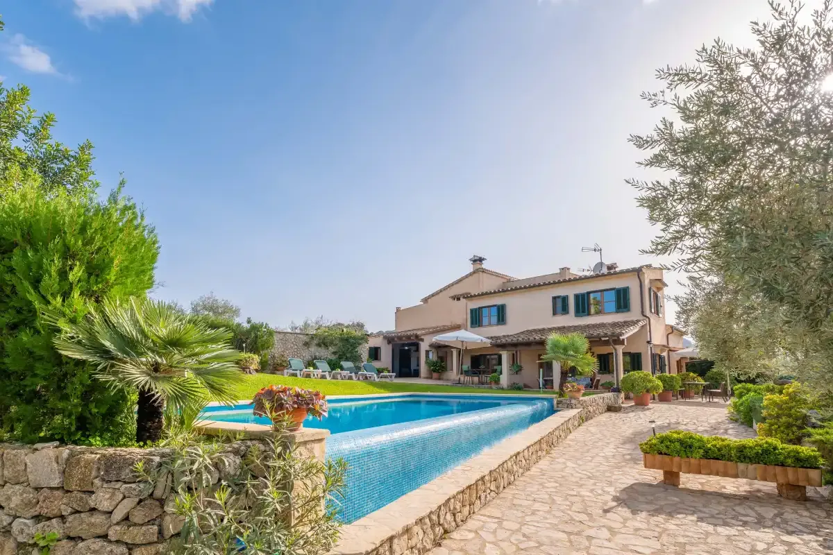 Una casa de estilo mediterráneo junto a una piscina y un patio pavimentado.