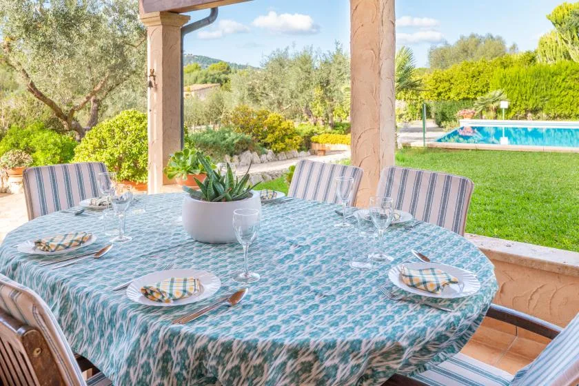 Una zona de comedor exterior cubierta da a un jardín y una piscina.