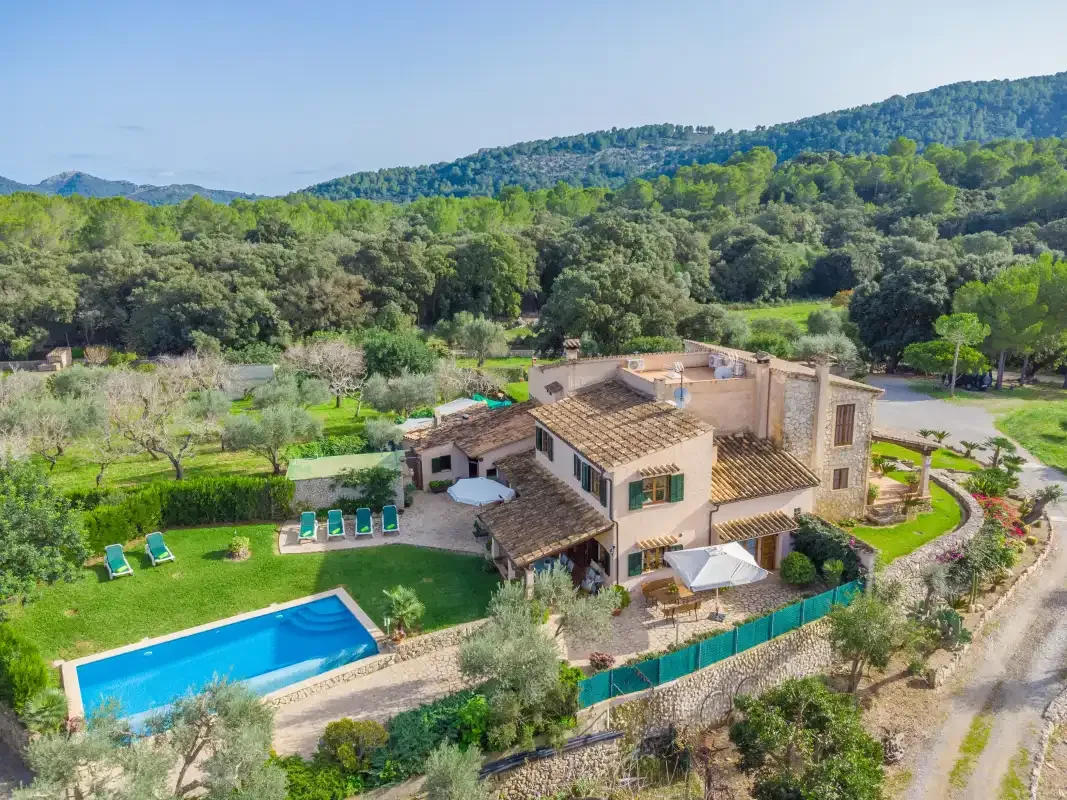 Una casa rural con piscina se encuentra entre colinas verdes y árboles.