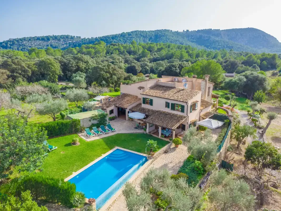 Una casa en el campo con piscina está rodeada de árboles y zonas verdes.