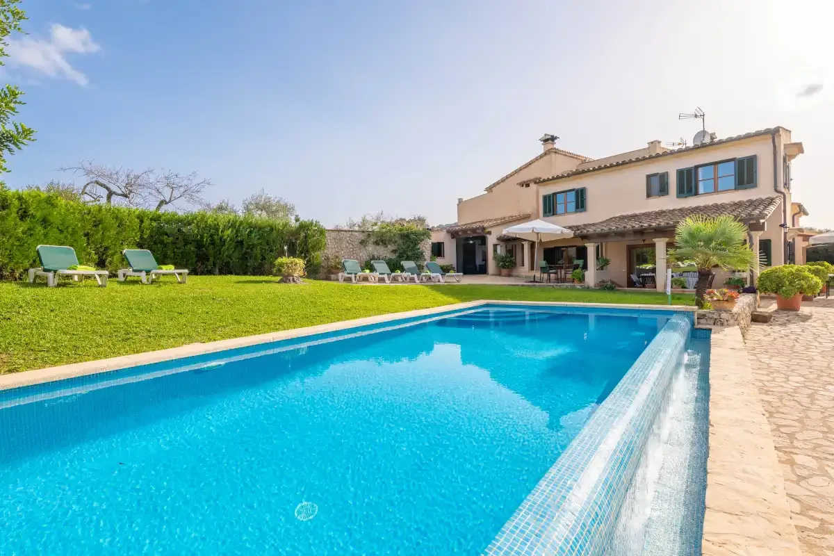 Una piscina junto a una casa, con césped y asientos al aire libre.