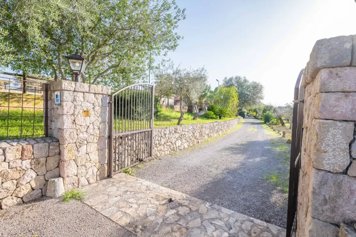 Una puerta metálica abierta da a un camino de grava bordeado por muros de piedra.