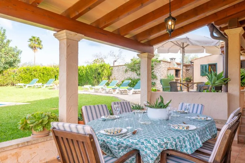 Una zona de comedor exterior cubierta con mesa y asientos frente a un jardín.