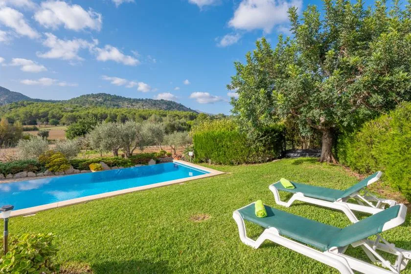 Una piscina al aire libre junto a un césped con tumbonas reclinables.